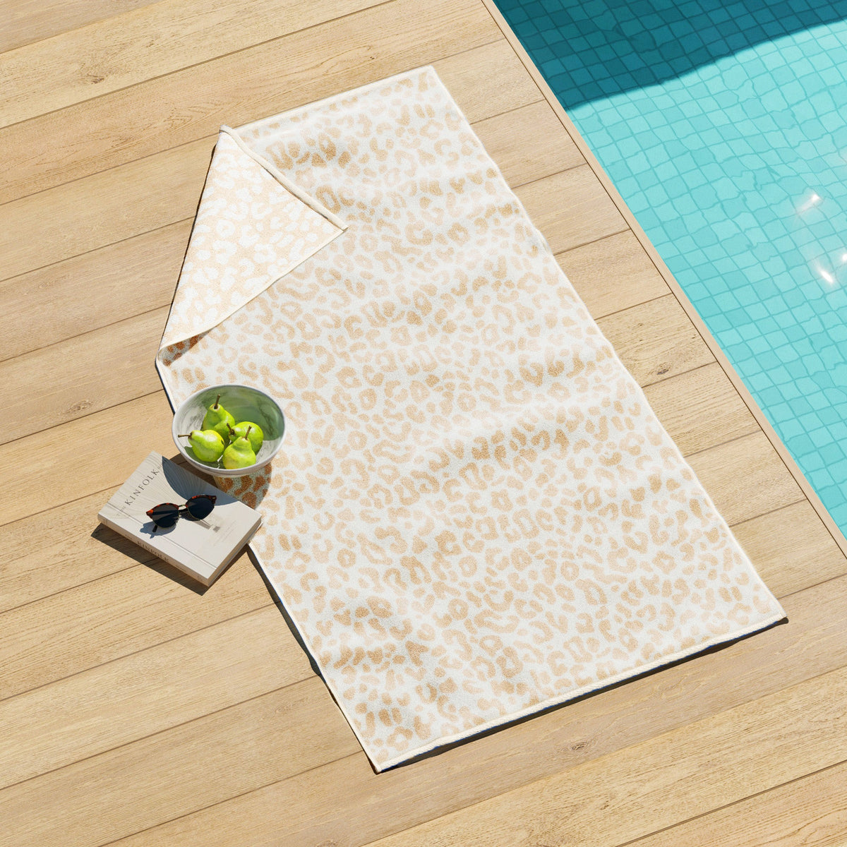 Maui Cotton Velour Beach Towel in vibrant green designs displayed on a chair by the beach.