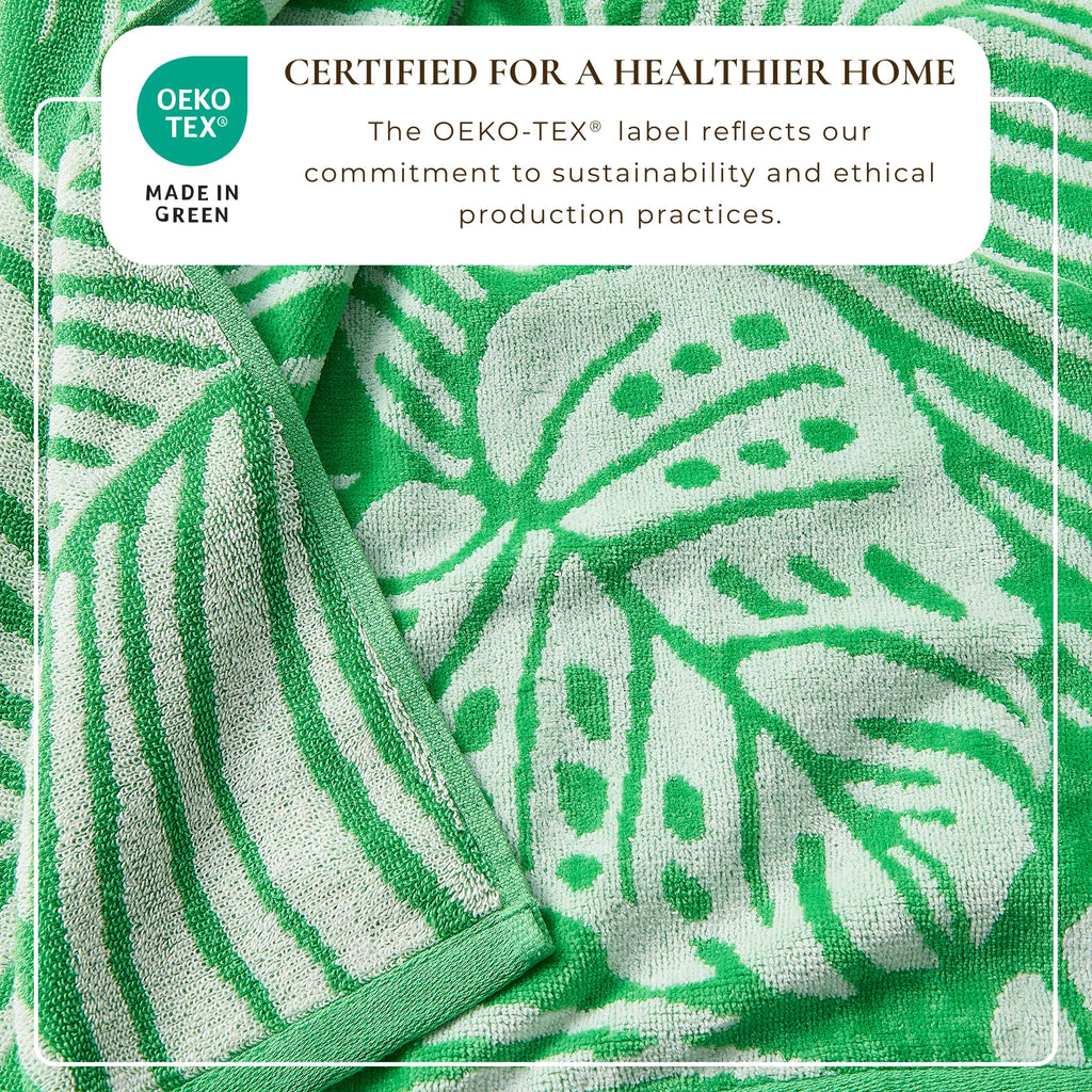 Maui Cotton Velour Beach Towel in vibrant green designs displayed on a chair by the beach.