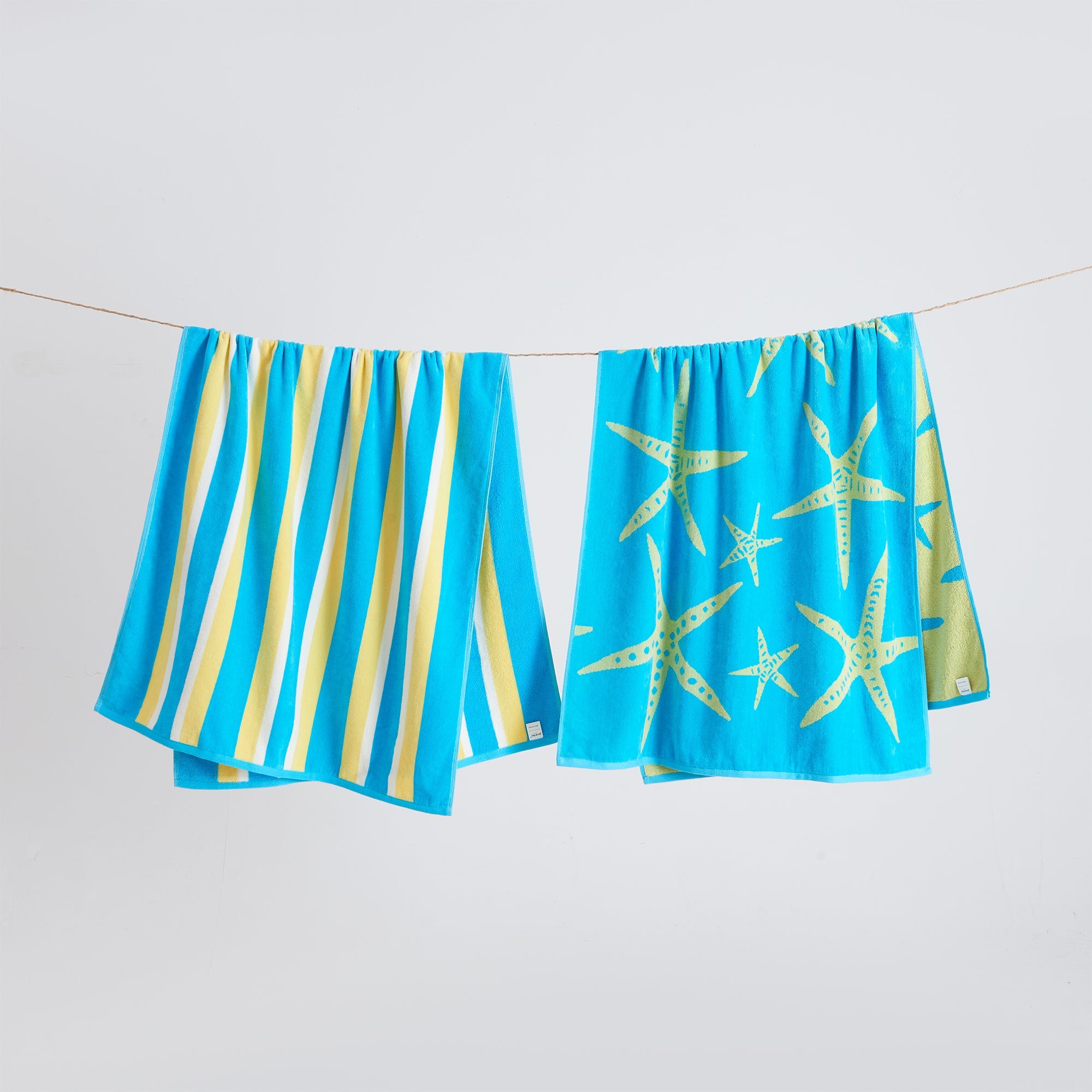 Maui Cotton Velour Beach Towel in vibrant green designs displayed on a chair by the beach.