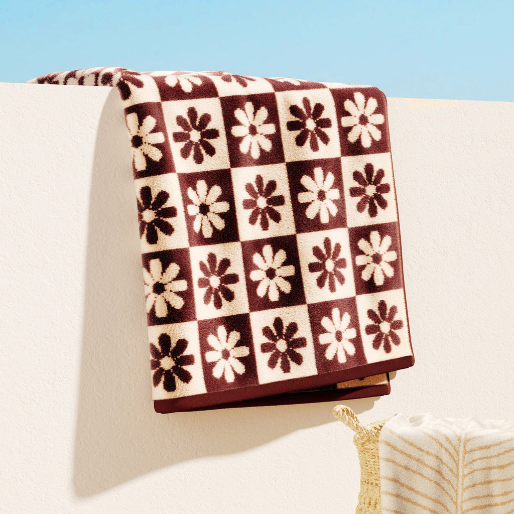 Maui Cotton Velour Beach Towel in vibrant green designs displayed on a chair by the beach.